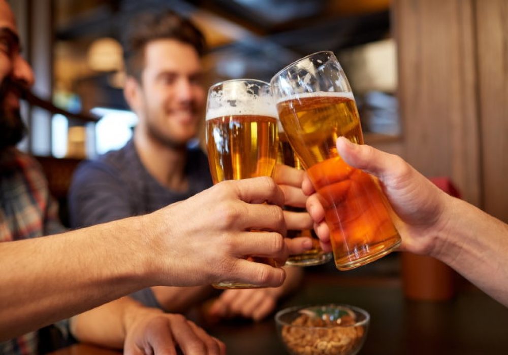 people, men, leisure, friendship and celebration concept - happy male friends drinking beer and clinking glasses at bar or pub